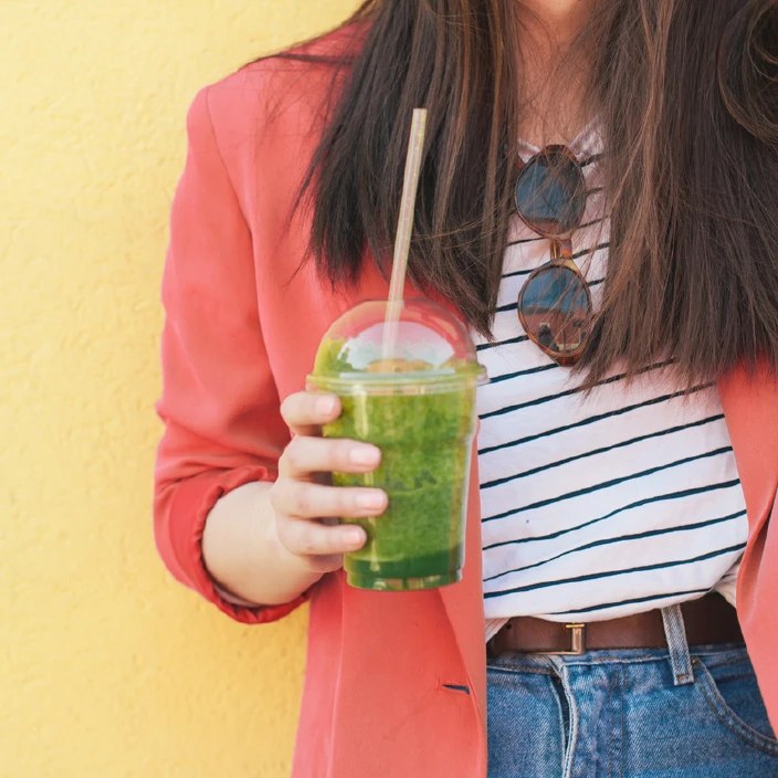 A woman in a colorful jacket drinking a green smoothie